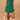Woman wearing a green dress holding a yellow bag against a beige background
