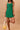 Woman wearing a green dress holding a yellow bag against a beige background
