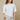 Woman wearing a white top with lace detail and patterned pants on a beige background