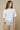 Woman wearing a white top with lace detail and patterned pants on a beige background