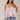 Woman wearing a light pink layered top and blue jeans against a neutral background
