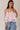 Woman wearing a light pink layered top and blue jeans against a neutral background