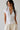Woman wearing a white blouse with lace details and beige pants against a plain background