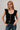 Woman wearing a black top with ruffled sleeves and blue jeans on a gray background