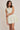 Woman wearing a light beige dress with floral patterns on a plain background