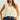 Woman wearing a cream-colored crochet vest over a white top and blue jeans on a light background