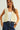 Woman wearing a cream-colored crochet vest over a white top and blue jeans on a light background