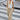 A woman walking across a city crosswalk wearing a white ribbed halter tank top and beige wide-leg jeans.