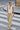 A woman walking across a city crosswalk wearing a white ribbed halter tank top and beige wide-leg jeans.